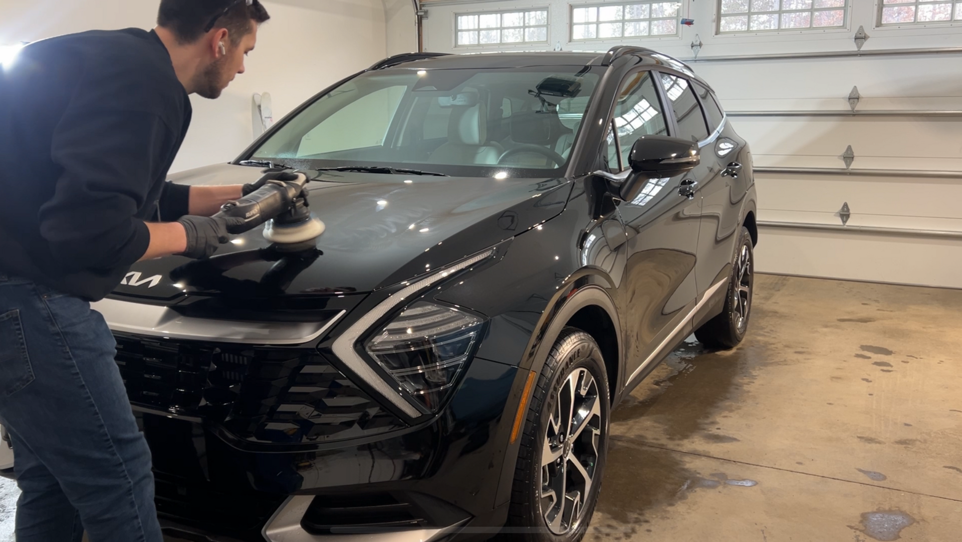 A man is polishing a black car in a garage.