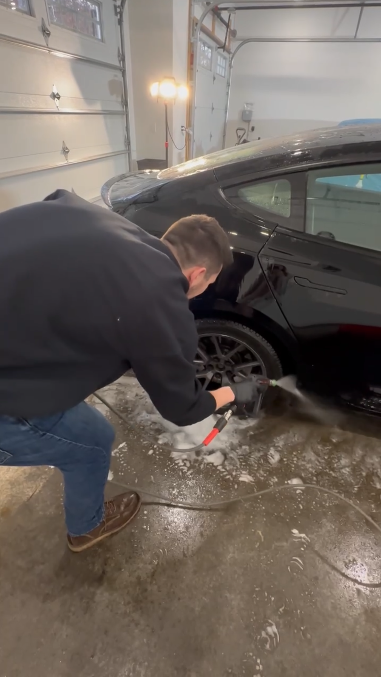 A man is washing a black car in a garage.