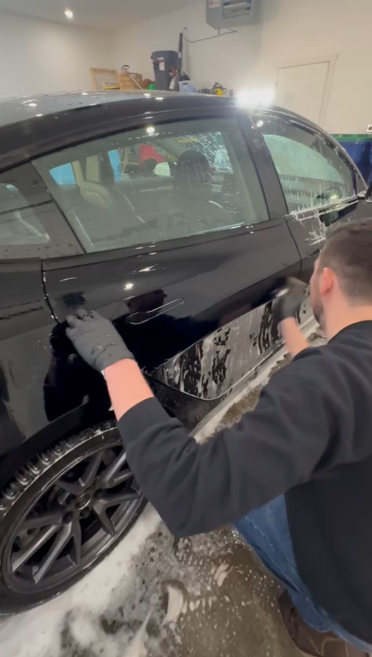A man is cleaning a black car in a garage.