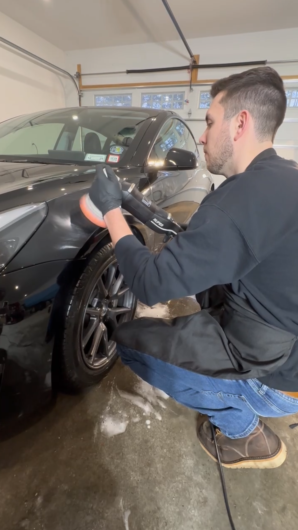 A man is kneeling down in a garage cleaning a car.