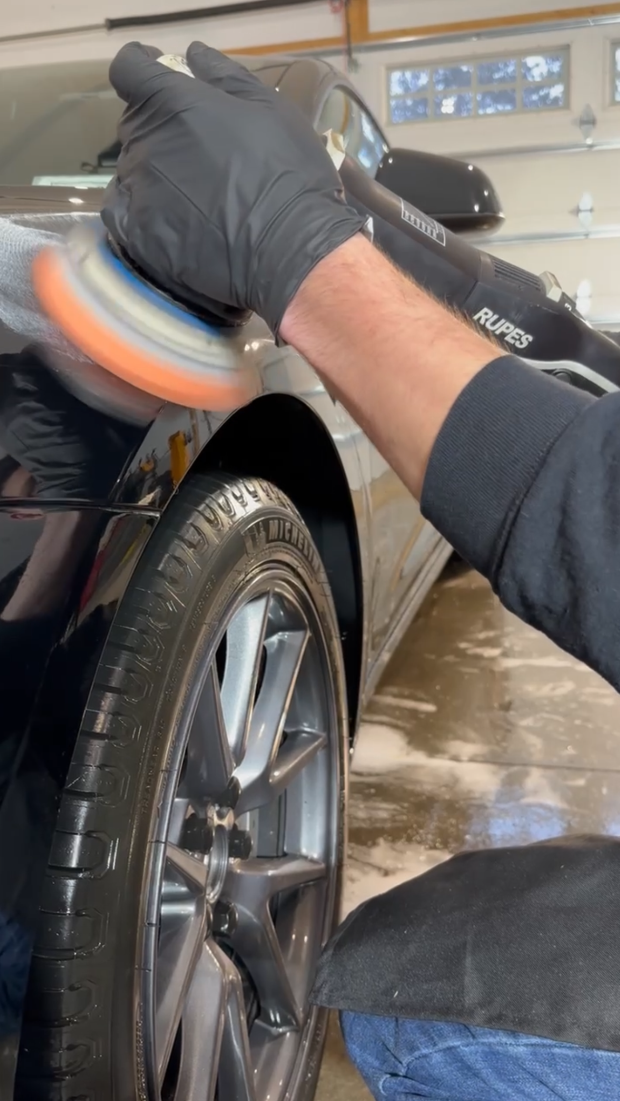 A man is polishing a car wheel with a polisher.