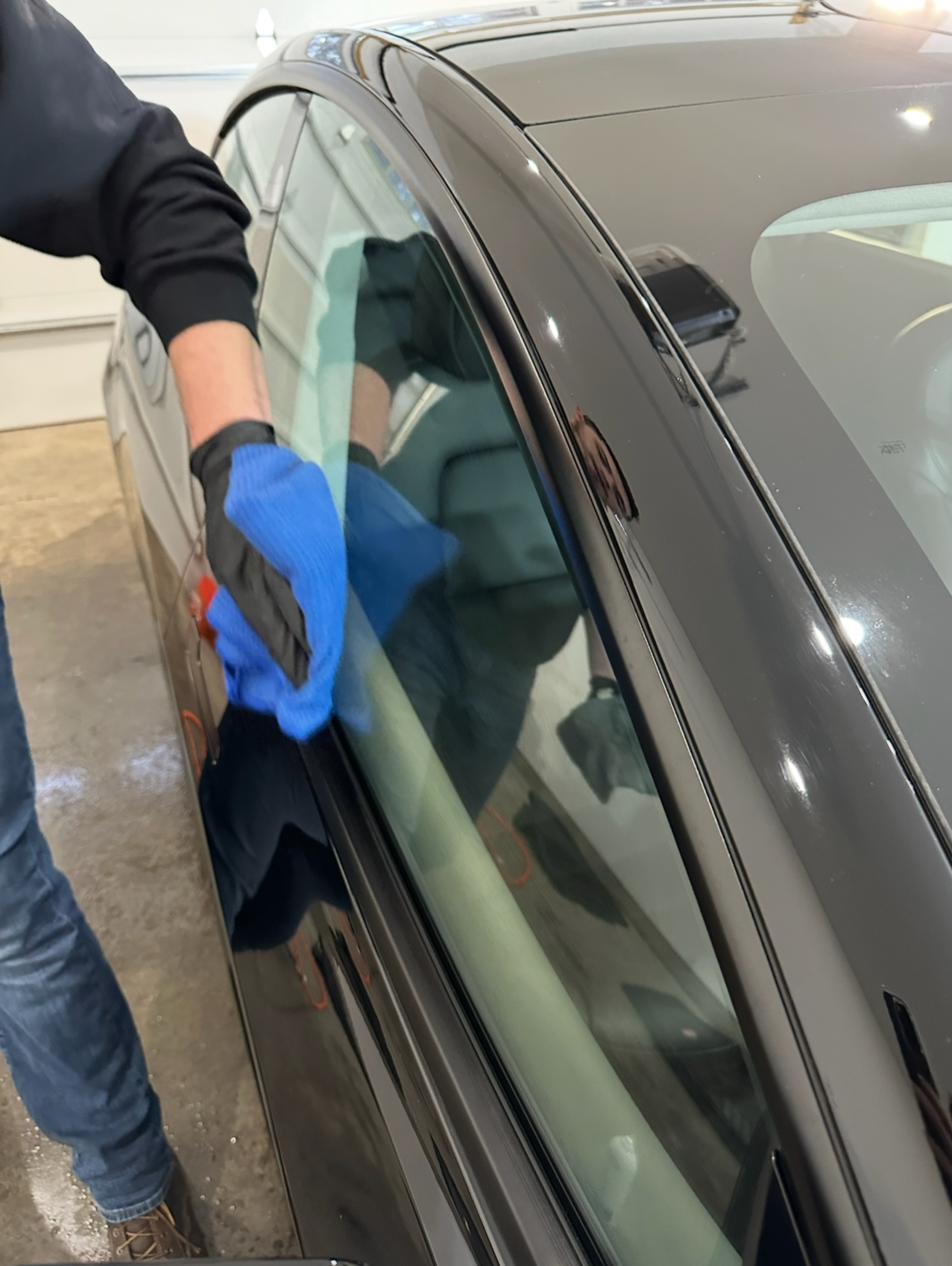A man wearing blue gloves is cleaning the windshield of a car