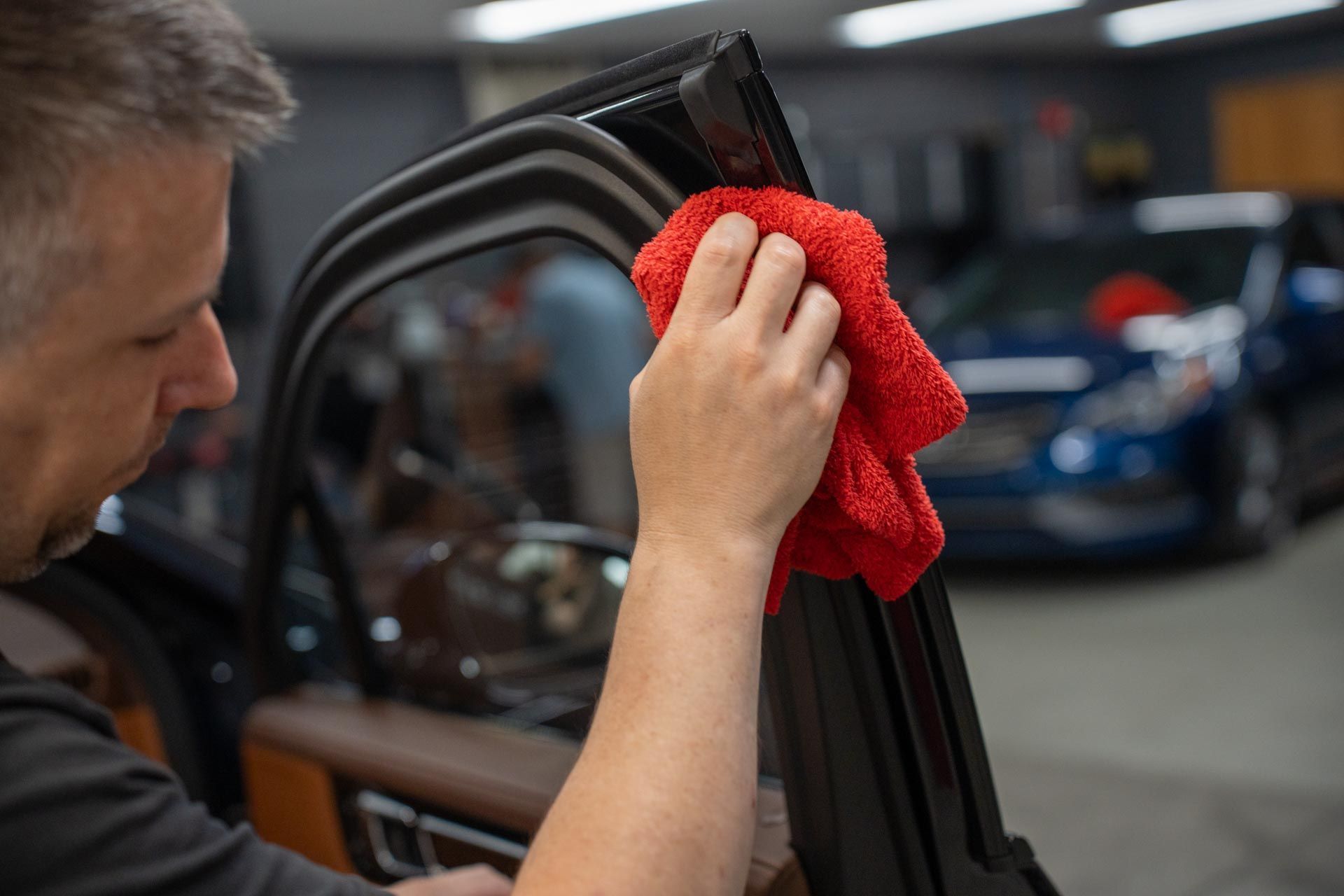 A man is cleaning the side of a car with a red towel.
