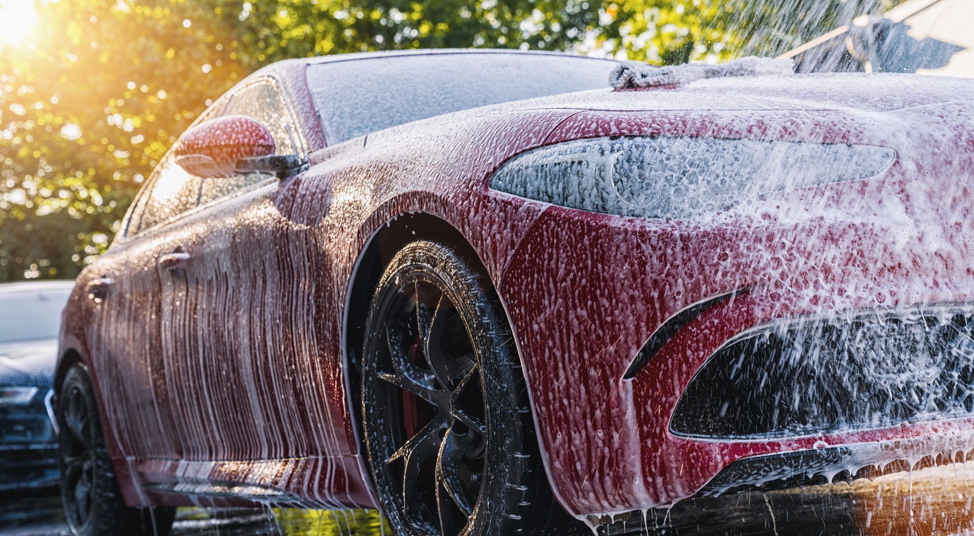 A red car is covered in foam while being washed.