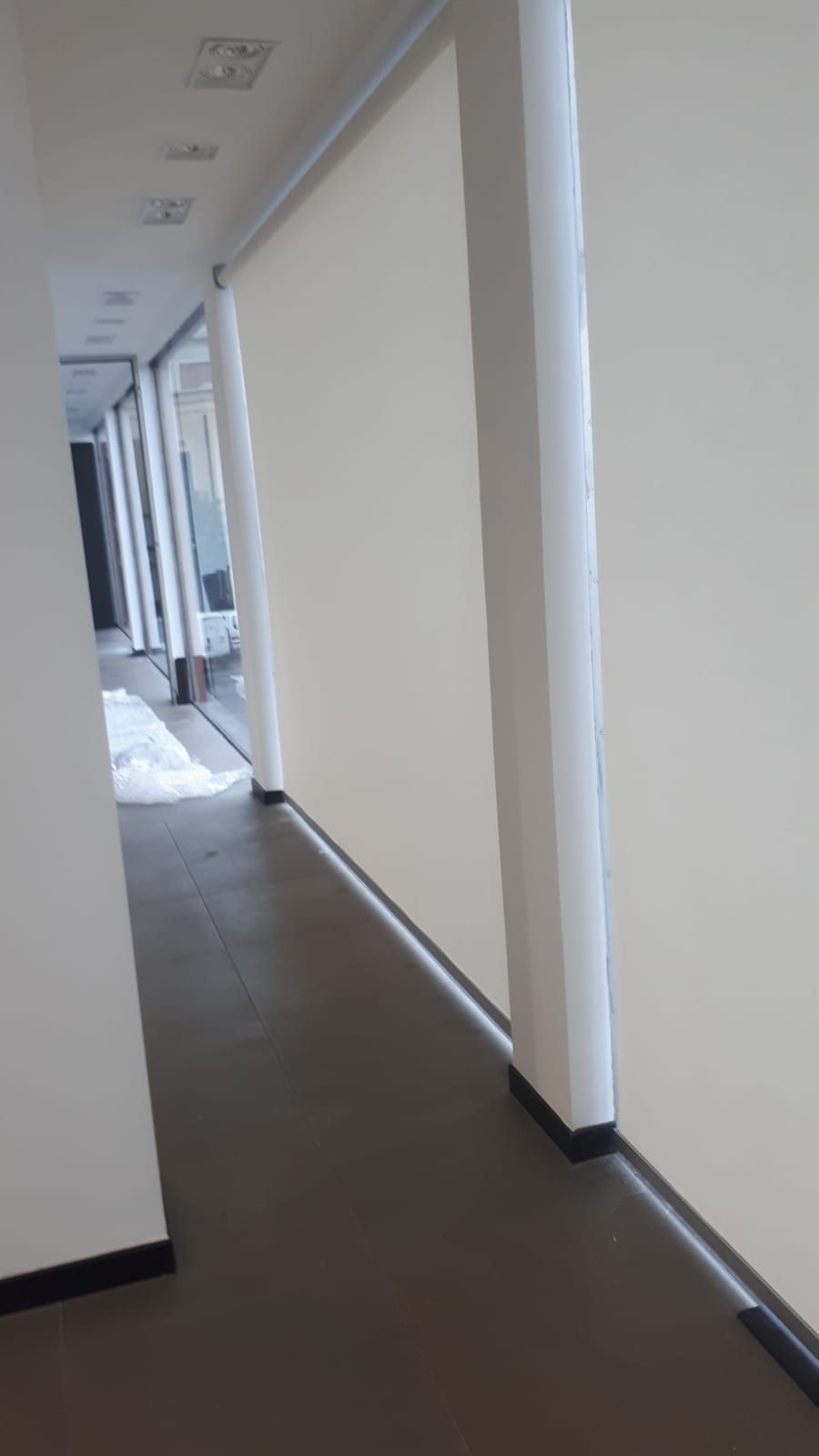 Un lungo corridoio con una parete bianca e un pavimento marrone