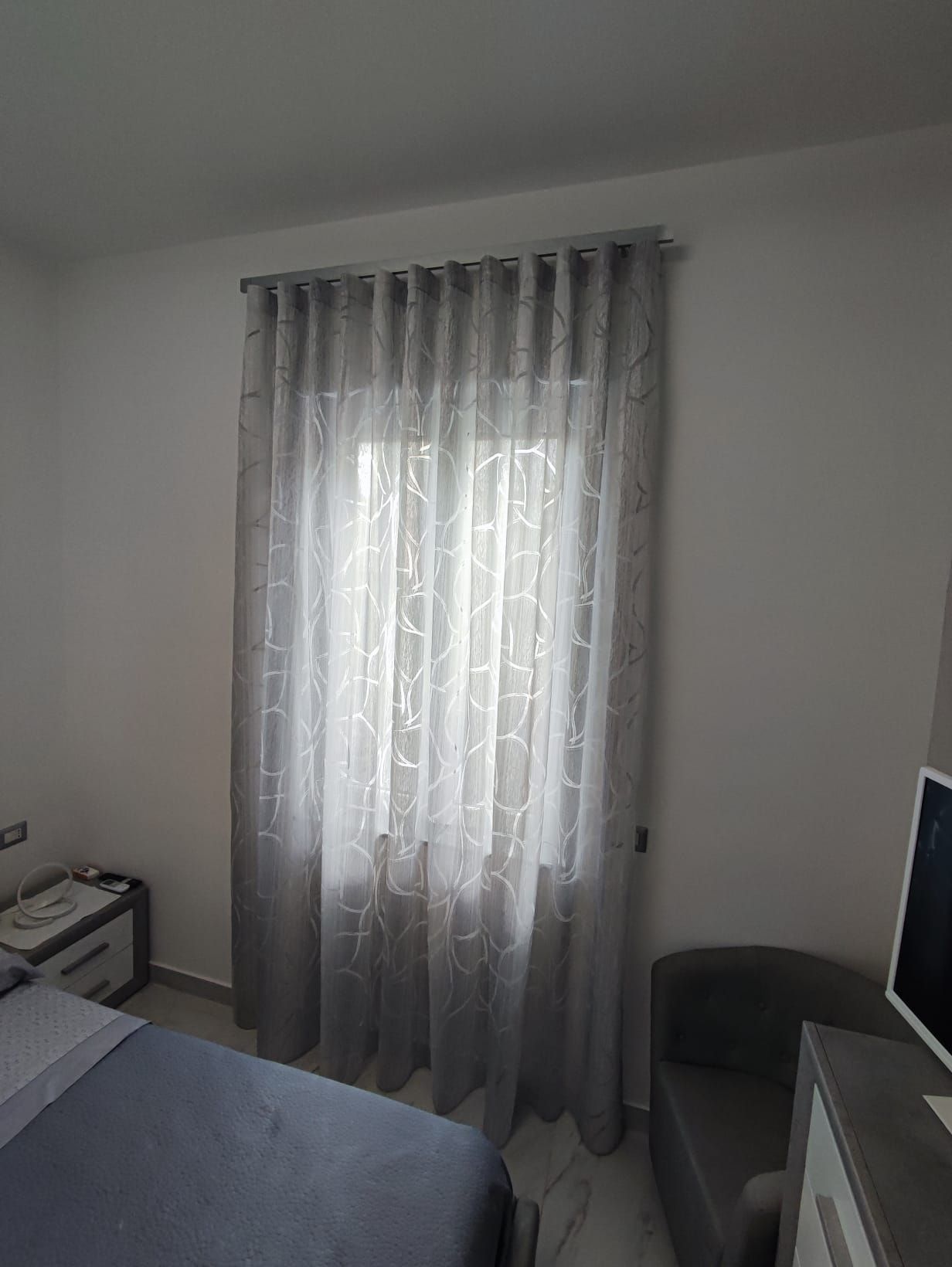 Una camera da letto con un letto, una sedia, un computer e delle tende.