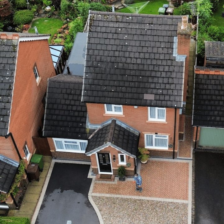 Aerial view of brick house with dark roof and paved driveway.