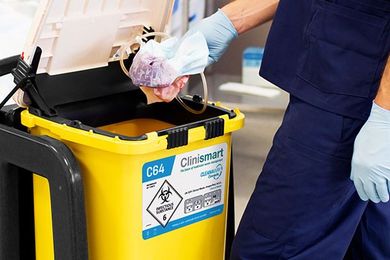 A person is putting a mask in a yellow bin.