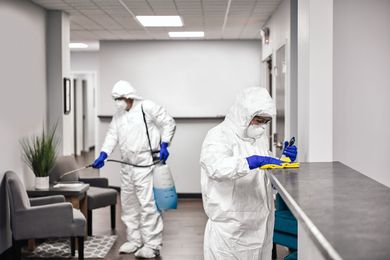 A couple of people in protective suits are cleaning a room.
