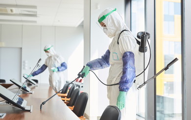 Two people in protective suits are disinfecting a conference room.