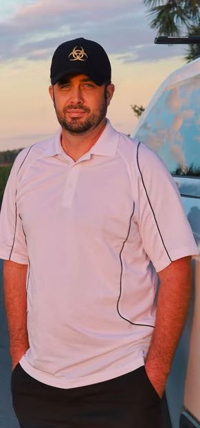 A man wearing a black hat and a white shirt is standing in front of a car