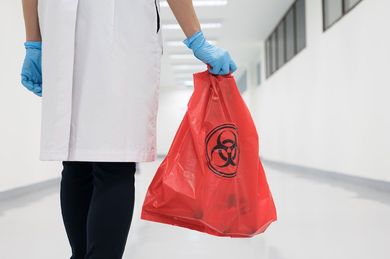 A doctor is holding a red biohazard bag in a hospital hallway.