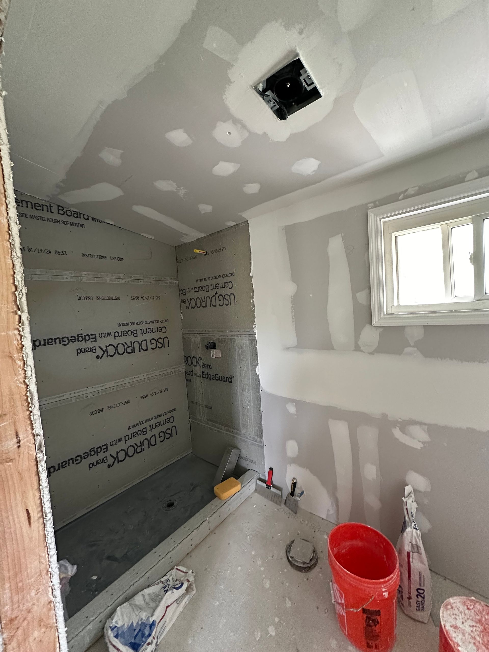 A bathroom under construction with buckets of paint and a window.