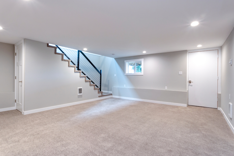 An empty basement with a staircase and a window.