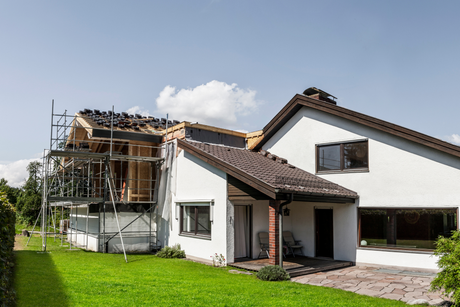 A white house with a brown roof is being remodeled.