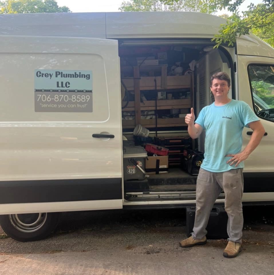 Man giving thumbs up next to a Gray Plumbing LLC van with open door.