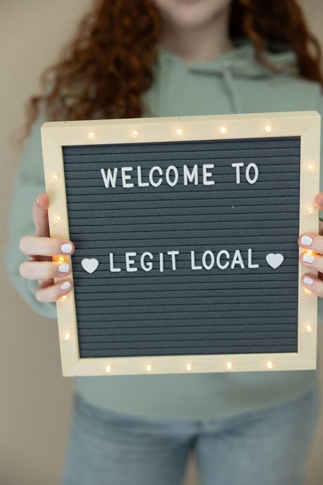 A woman is holding a sign that says `` welcome to legit local ''.