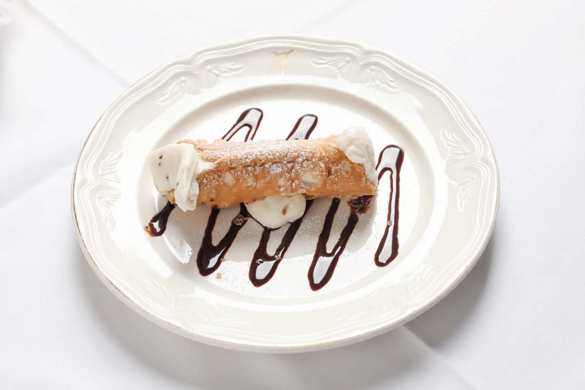 A white plate topped with a cannoli and chocolate sauce.
