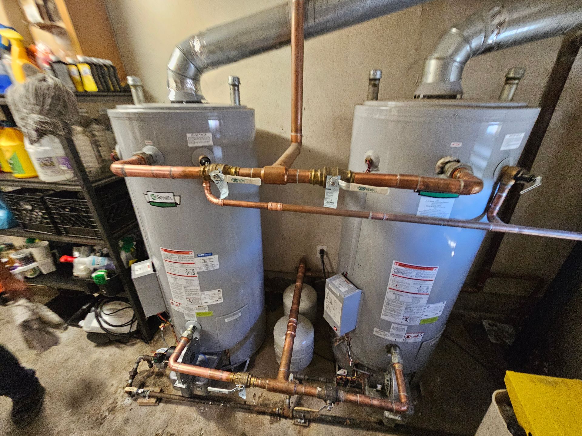 Two water heaters are sitting next to each other in a garage.