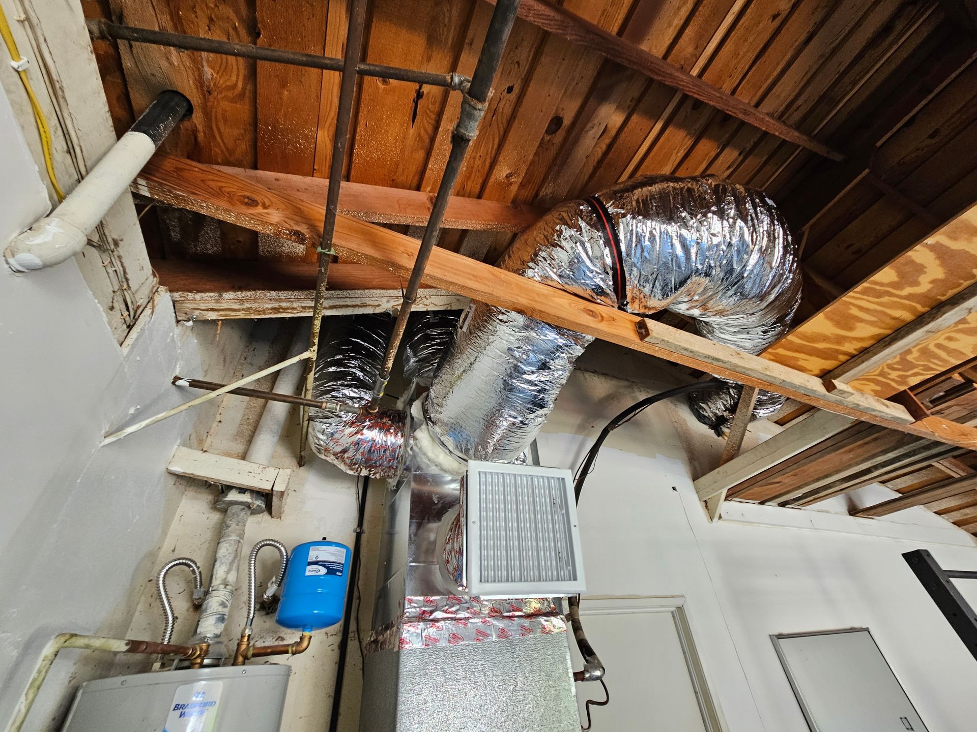 A room with a water heater , air conditioner , and pipes hanging from the ceiling.