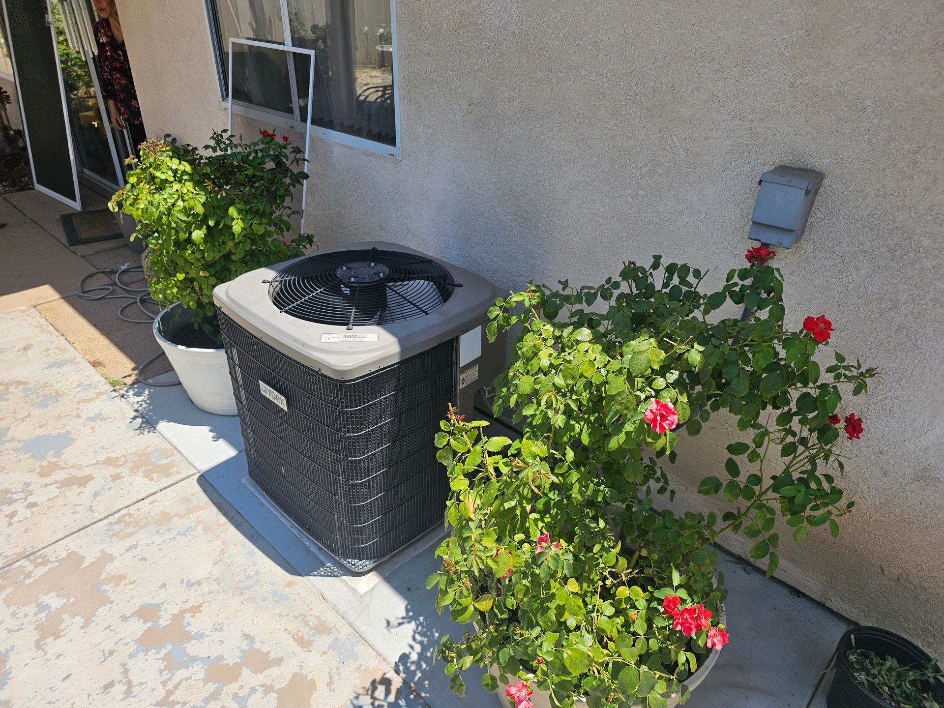 An air conditioner is sitting on a patio next to potted plants.