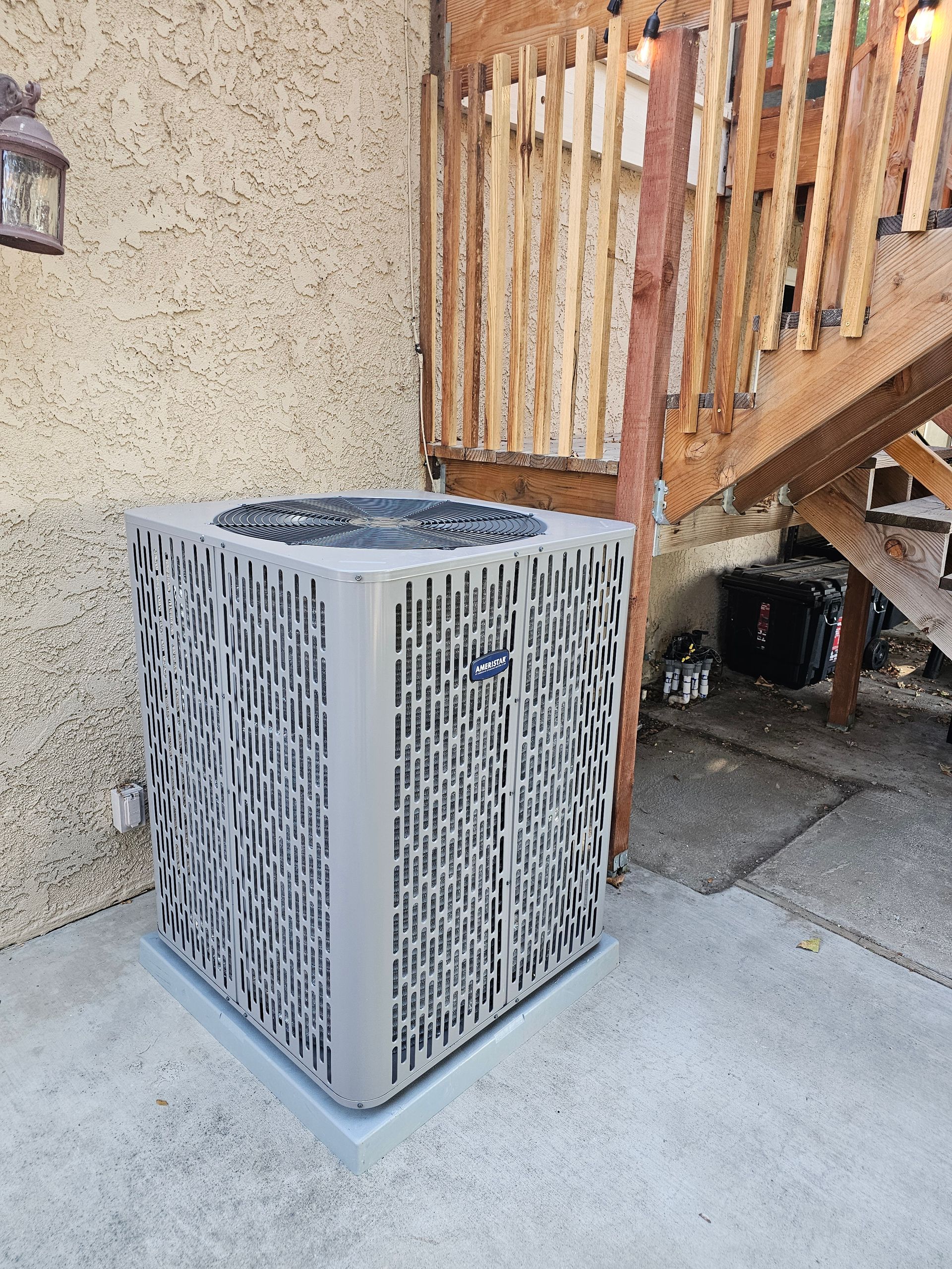 A large air conditioner is sitting on the side of a building next to stairs.