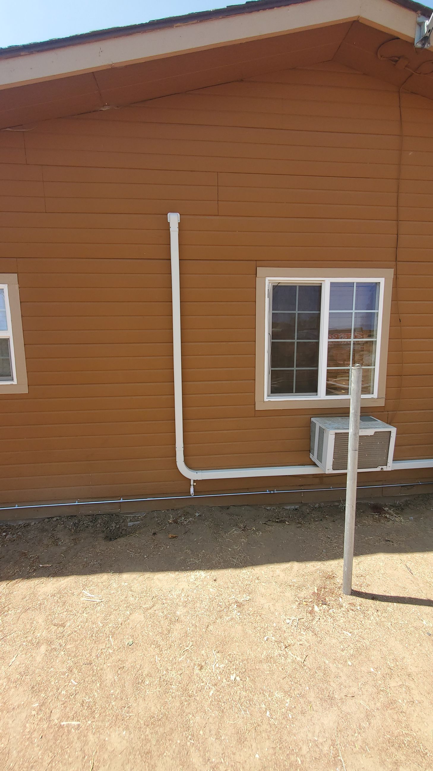A brown house with a window and an air conditioner on the side.