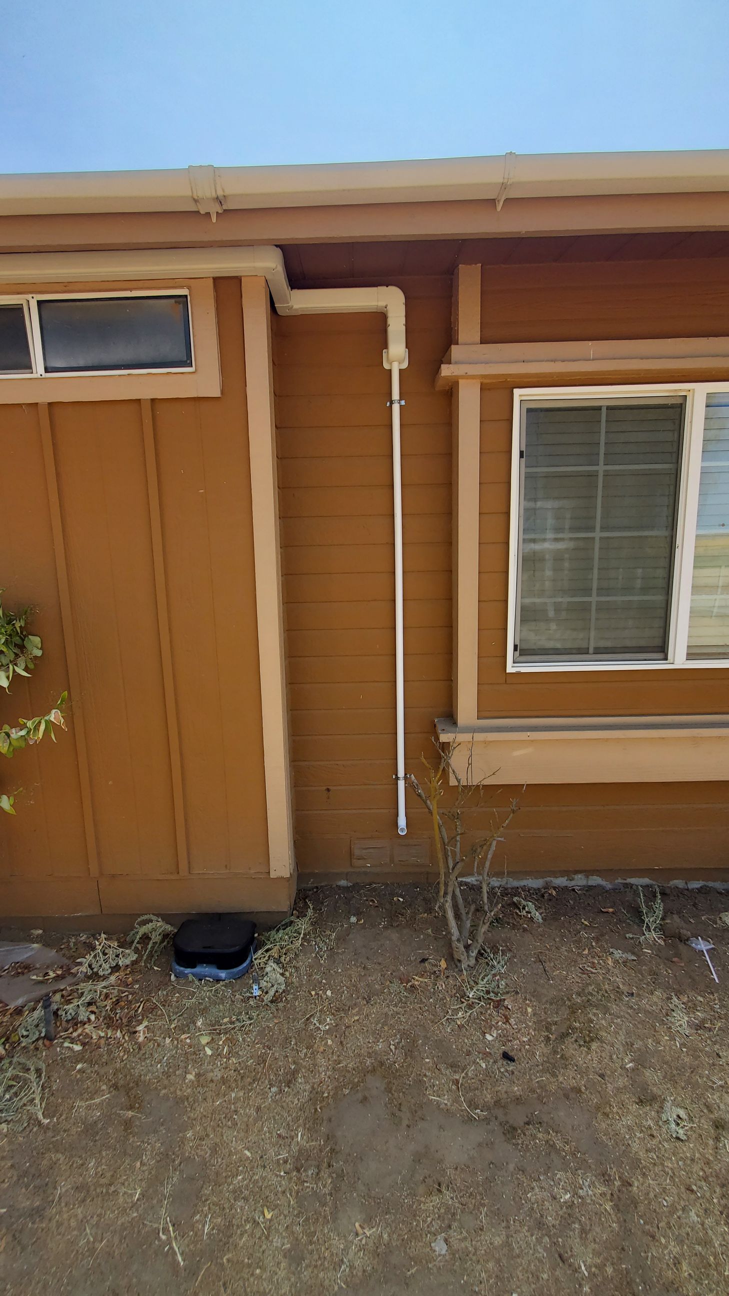 A brown house with a window and a pipe on the side of it.