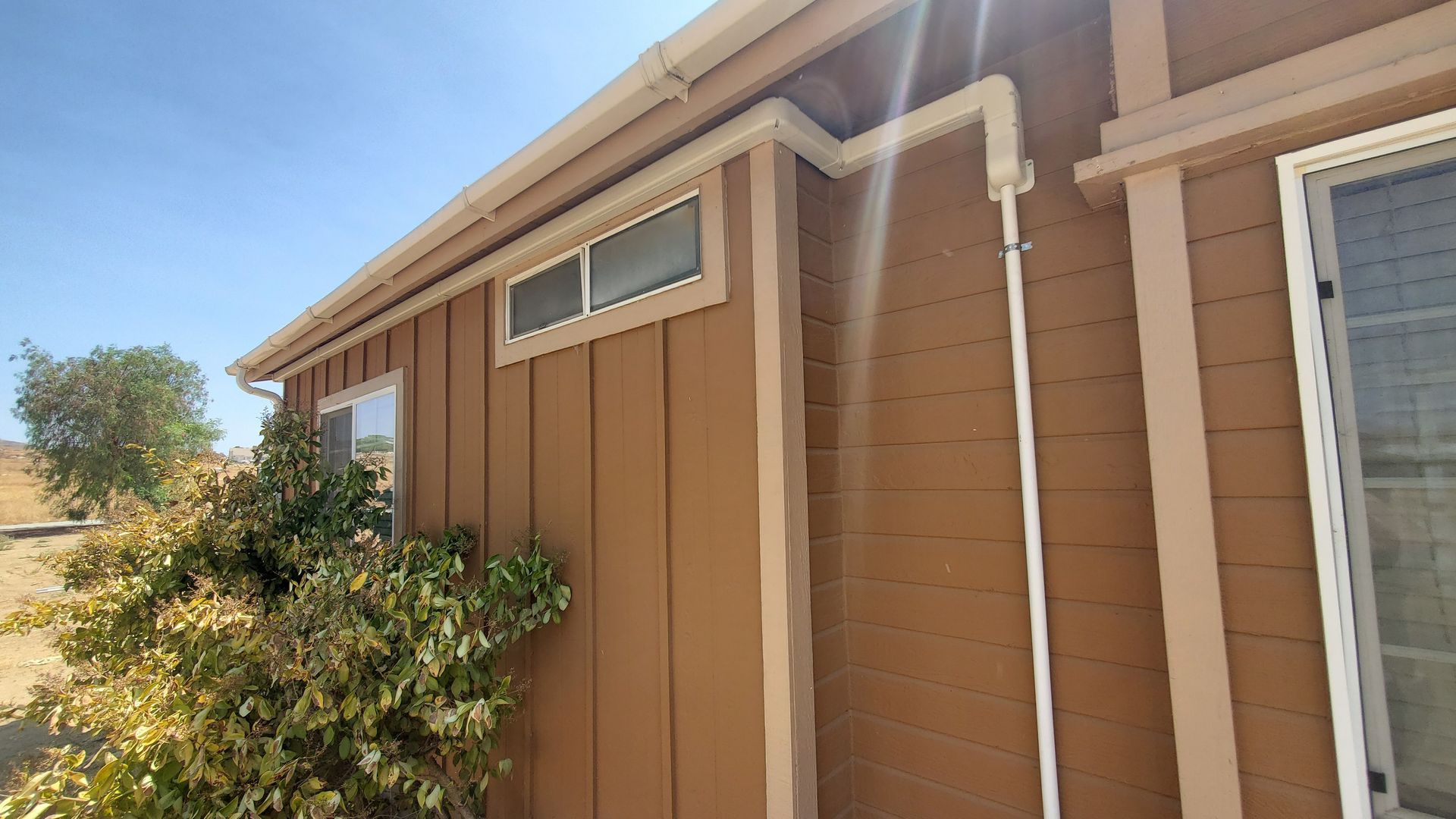A brown house with a white pipe on the side of it.