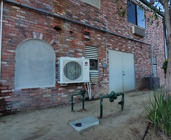 A white air conditioner is mounted on the side of a brick building.