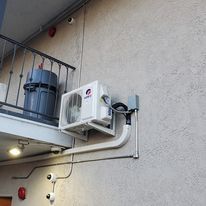 An air conditioner is mounted on the side of a building next to a balcony.
