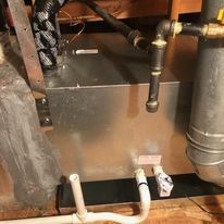 A close up of a water heater in a basement with pipes coming out of it.