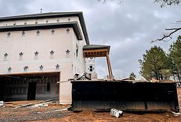 A large bulldozer is parked in front of a house under construction.