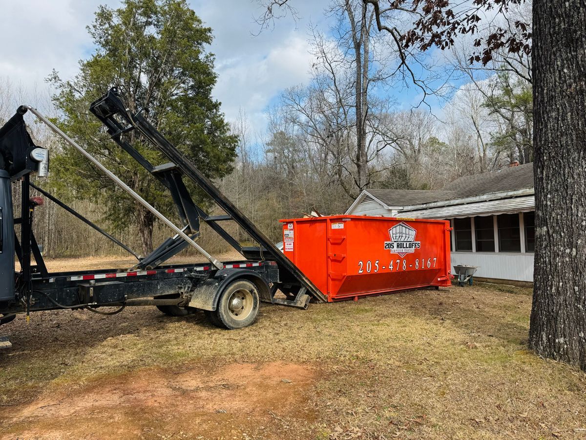 A dumpster is sitting on top of a trailer in front of a house.