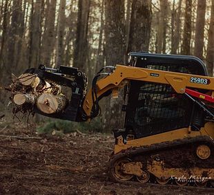 A bulldozer is carrying a pile of logs in the woods.