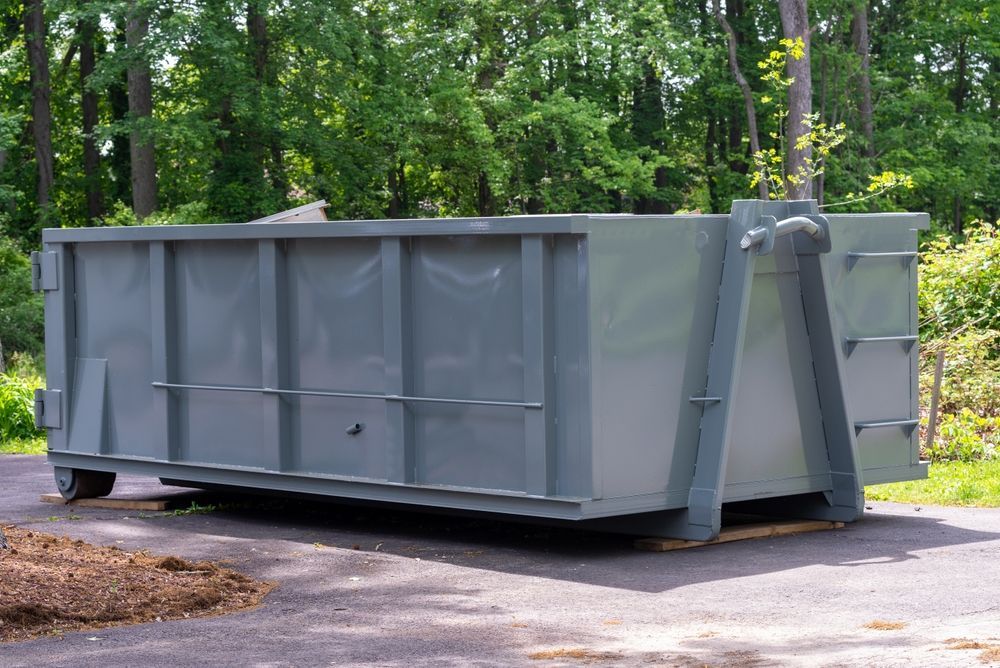 A large gray dumpster is parked on the side of a road.