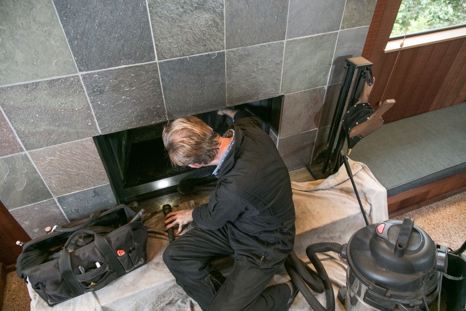 A man is working on a fireplace with a vacuum cleaner.