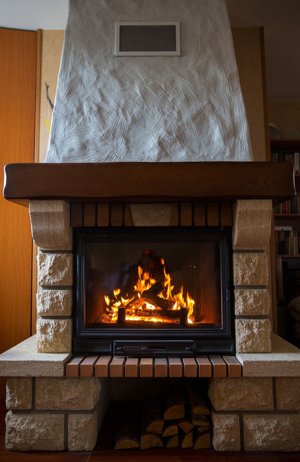 Fireplace with burning logs, stone facade, and wooden mantel. Warm interior setting.