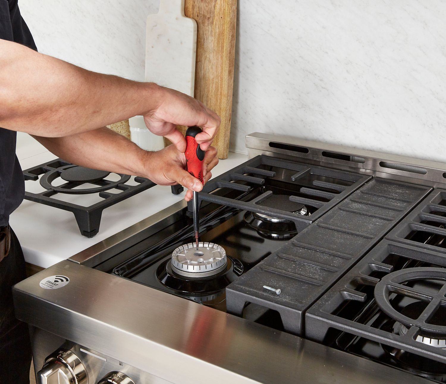 A man is fixing a stove with a screwdriver.