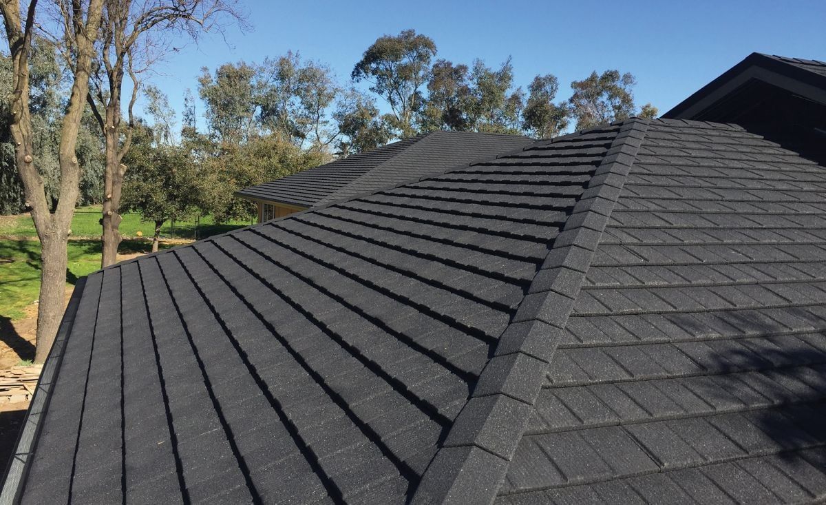 Dark gray asphalt shingle roof on a house, with trees in the background on a sunny day.