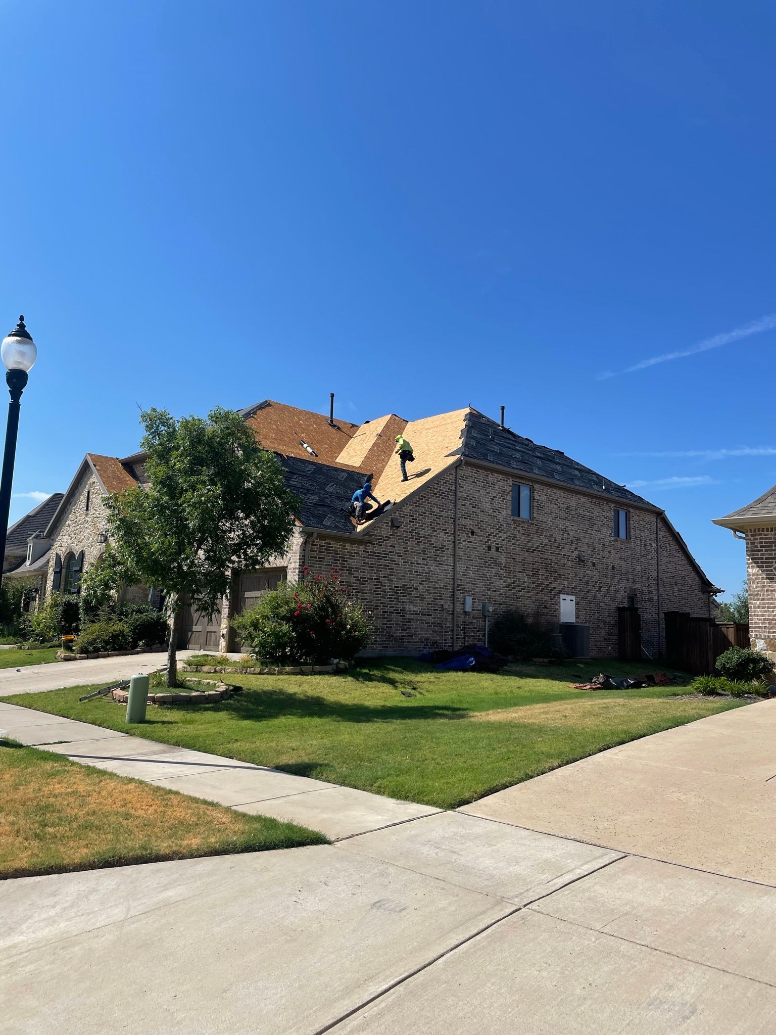 House with roof being replaced; workers on roof, sunny day.