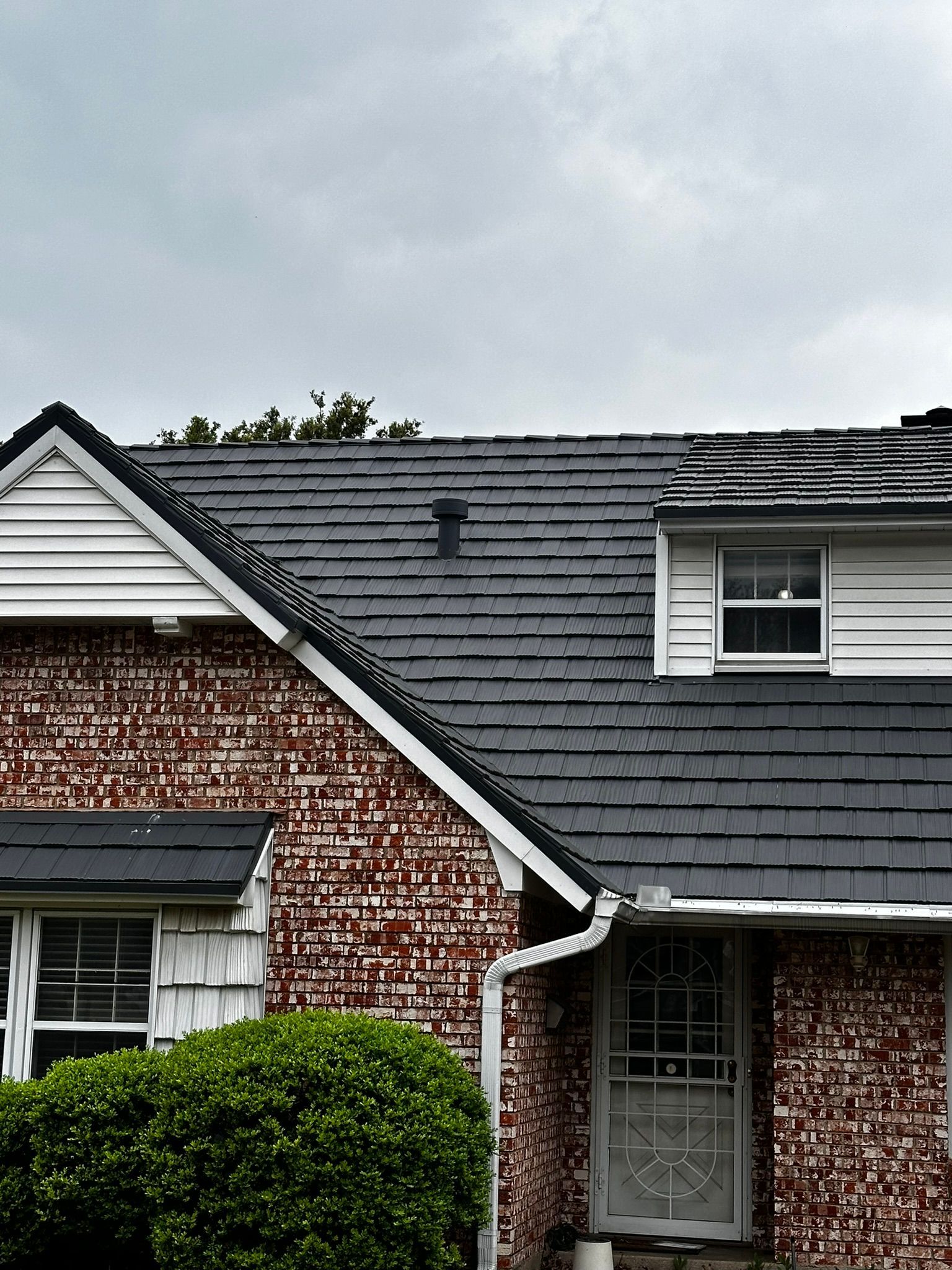 House with brick siding, dark roof, and cloudy sky.