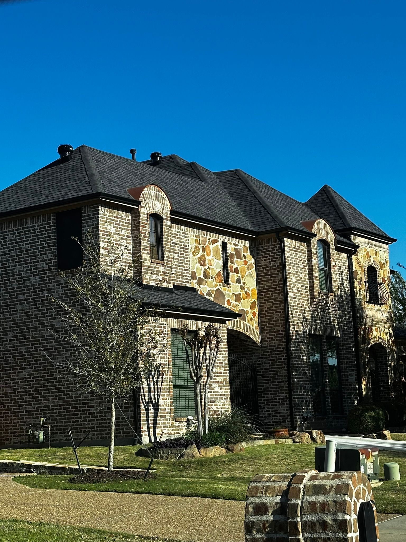 Two-story brick and stone house under a blue sky.