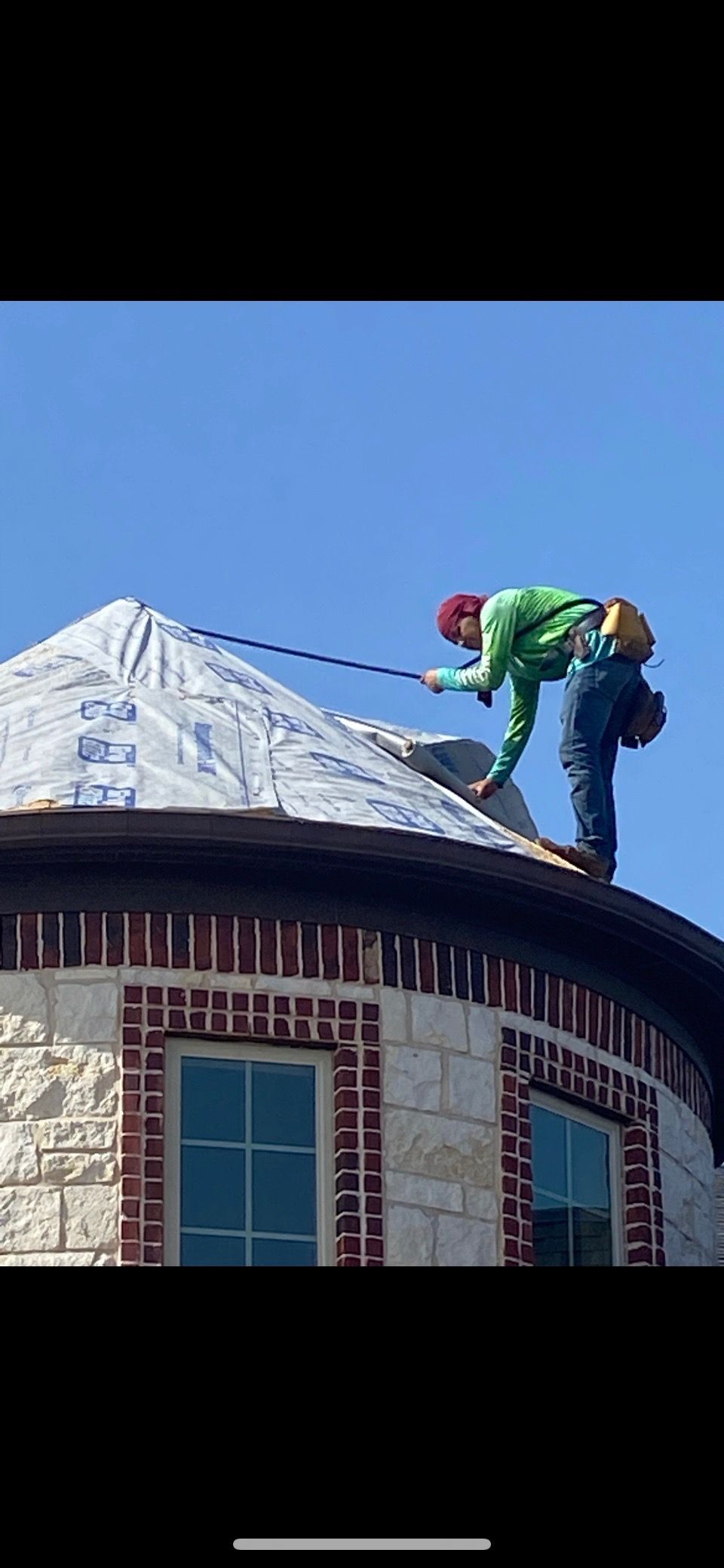 Two roofers on a round, brick-trimmed roof, working under a clear blue sky.