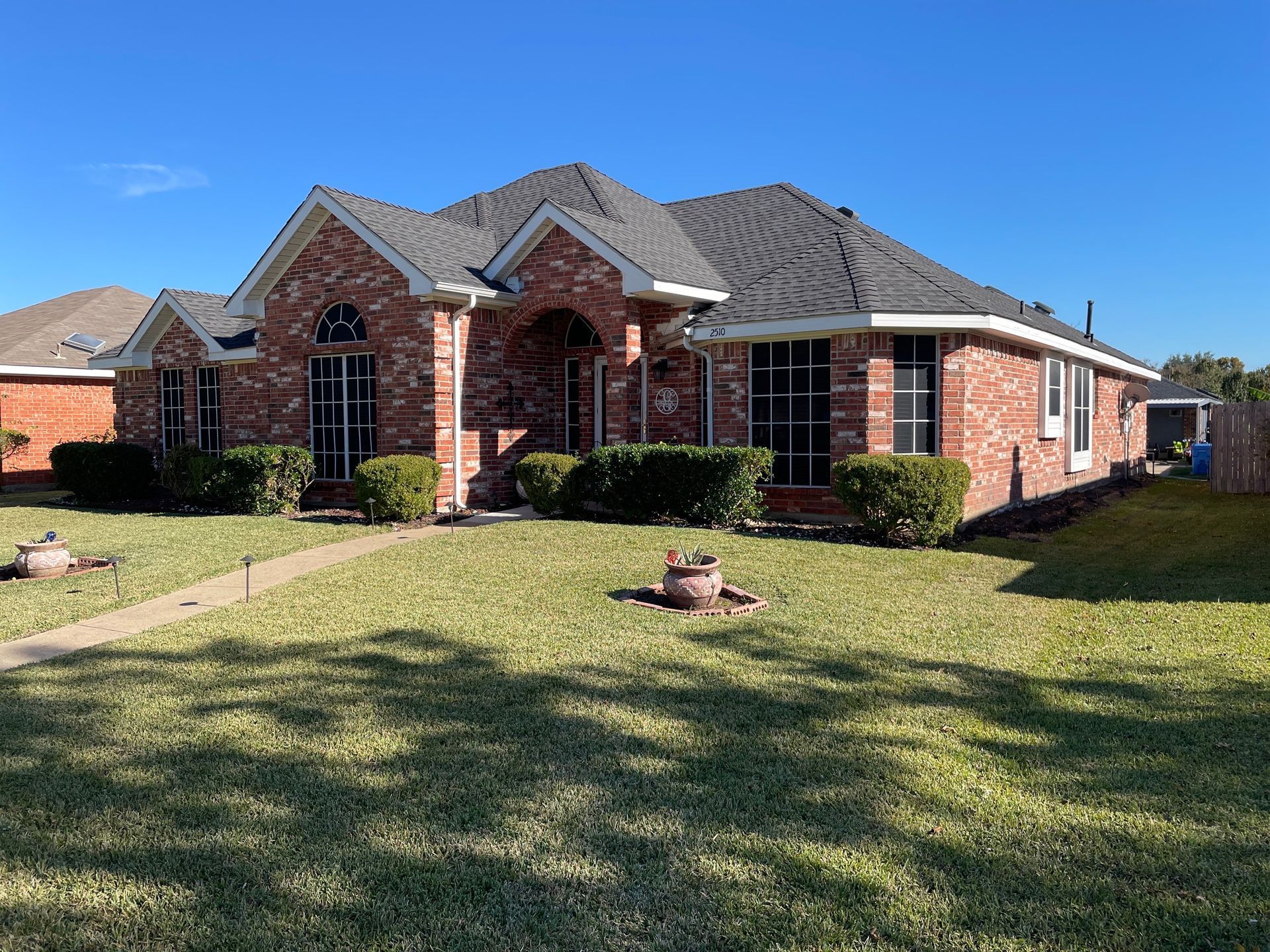 Brick house with a dark roof, green lawn, and blue sky.