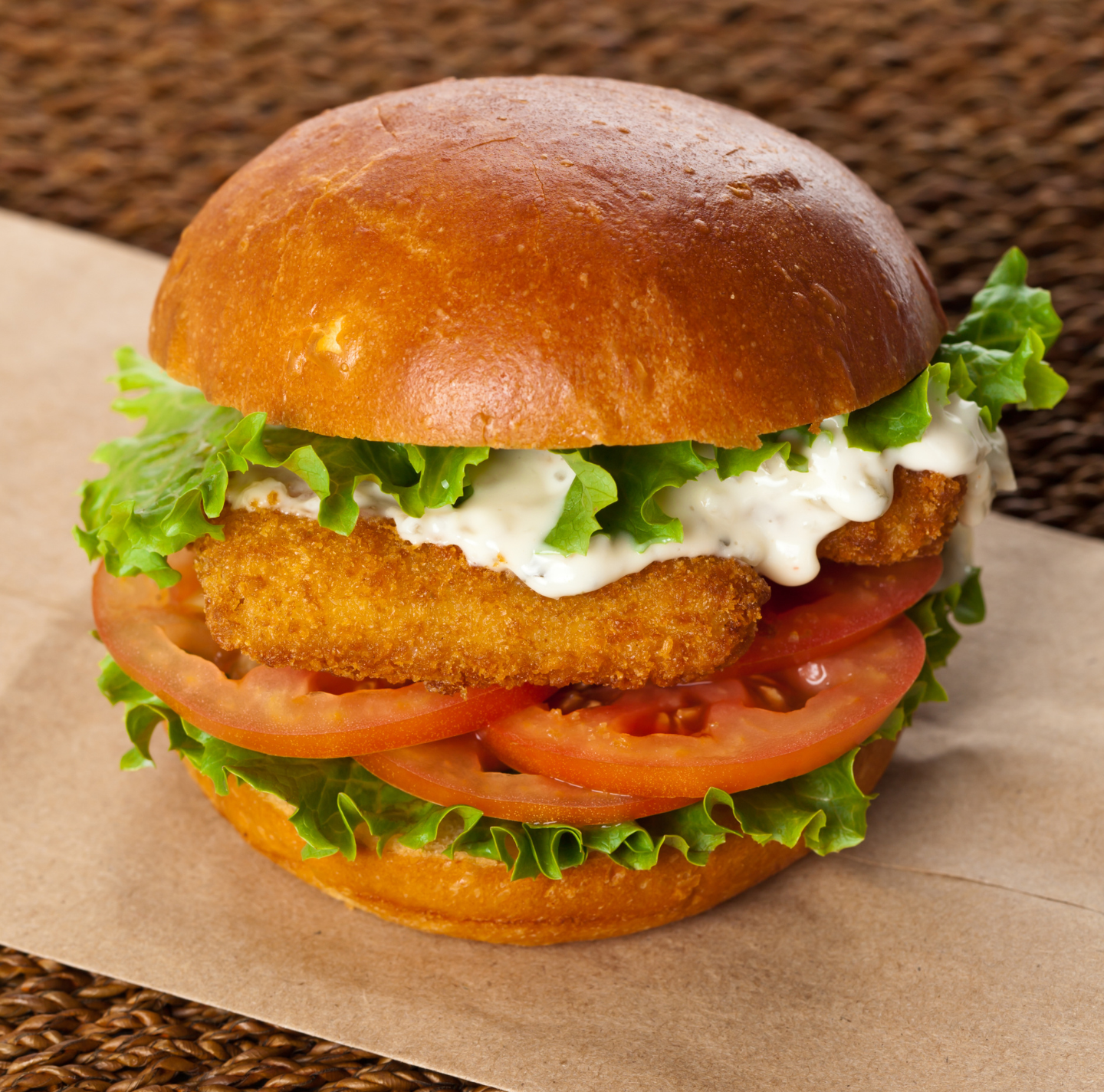 A fried fish sandwich with lettuce tomatoes and mayonnaise on a bun