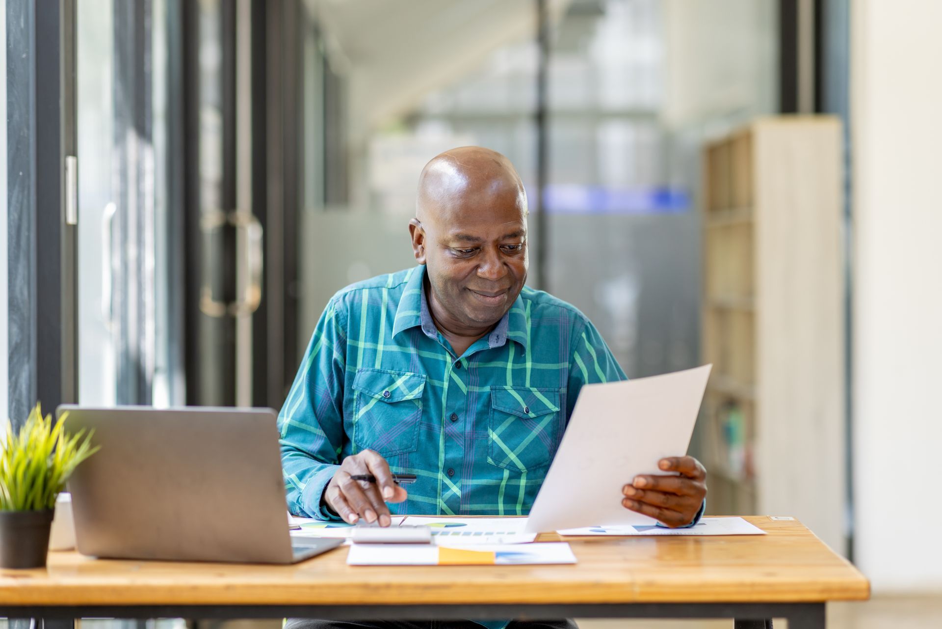 A man is sitting at a desk with a laptop and a piece of paper.