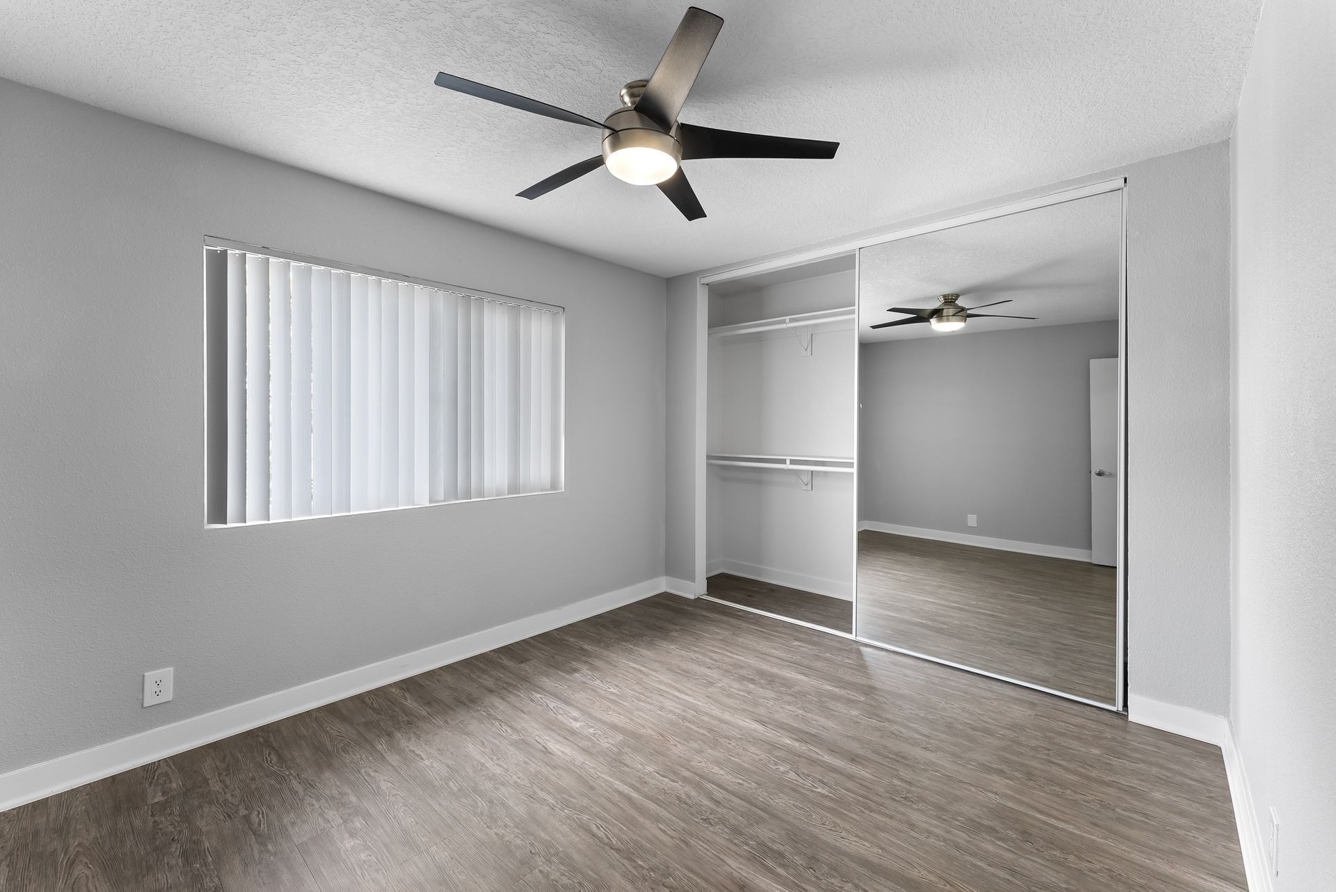 An empty bedroom with a ceiling fan and a large mirror.