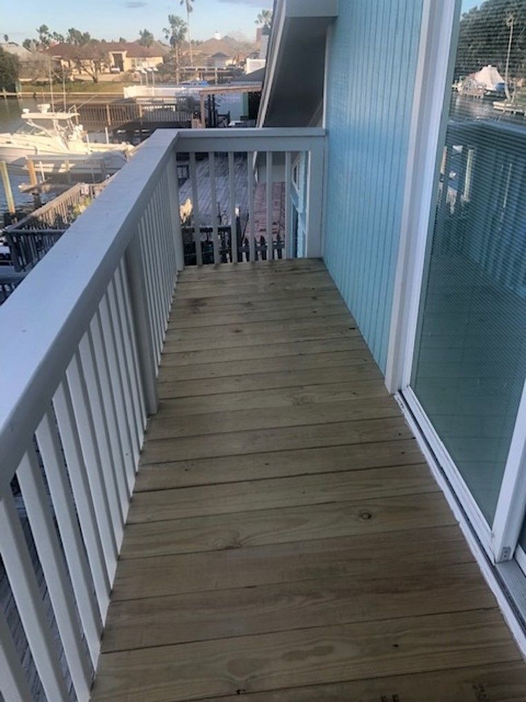 a balcony with a wooden deck and a white railing . | Corpus Christi, TX | GT Roofing