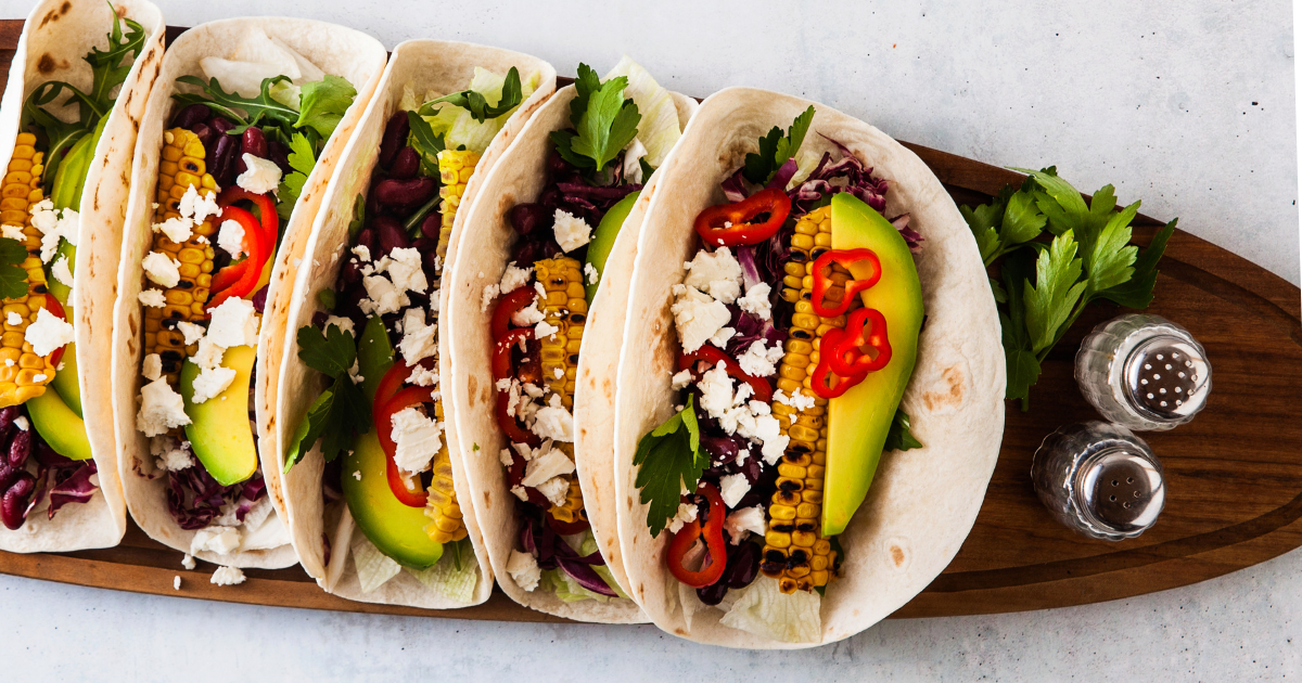 A wooden cutting board topped with a row of breakfast tacos.